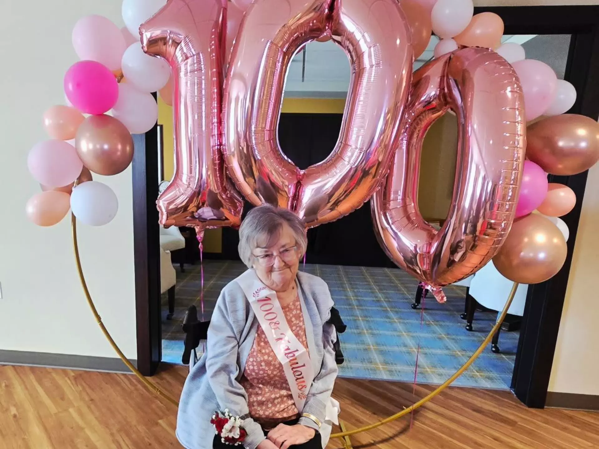 A StoryPoint Group centenarian is posing in front of pink birthday balloons, which are in the shape of the number 100.